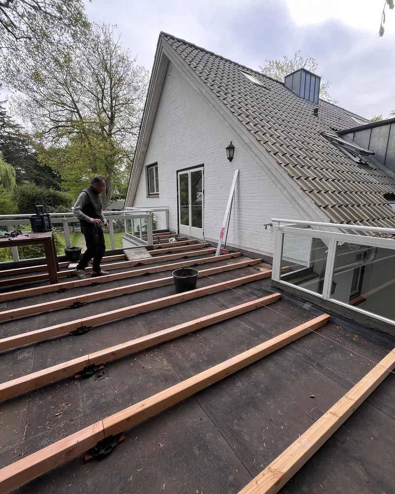 Zimmerer verlegt die Lagerhölzer einer Terrasse auf abgedichtetem Untergrund