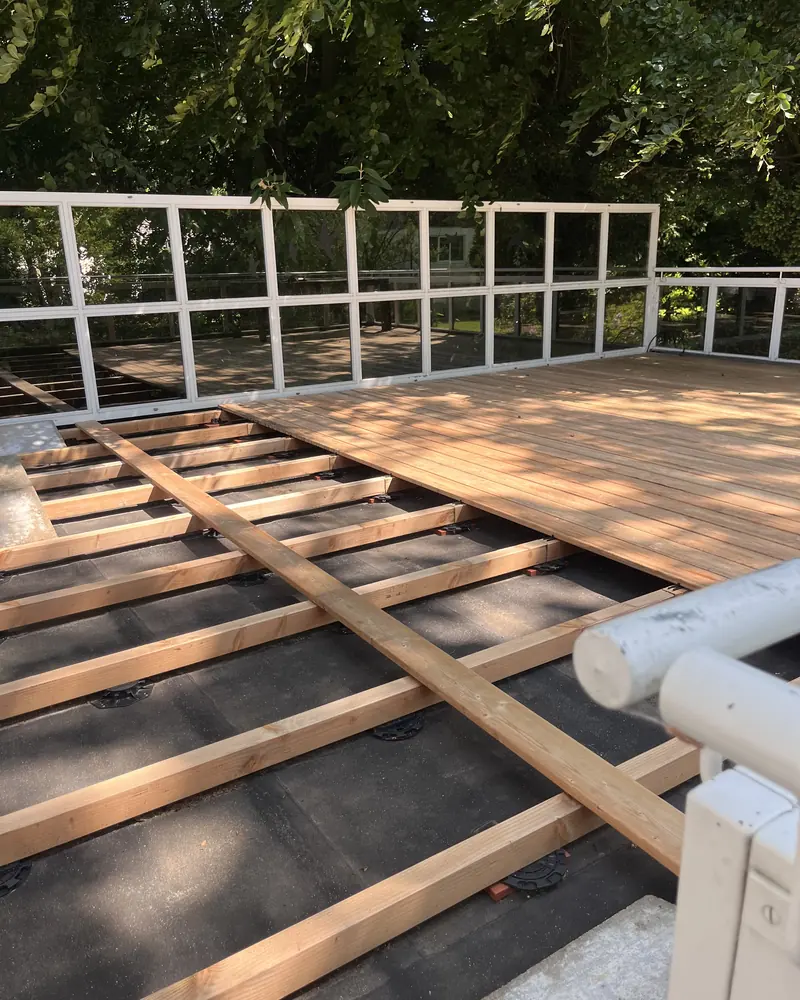 Halb verlegte Terrassendielen auf der Unterkonstruktion, dahinter ein Glasgeländer