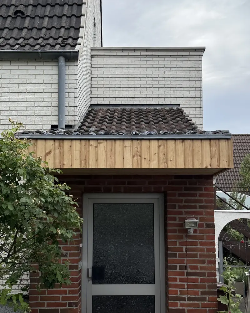Vordach mit senkrechter Holzverkleidung über dem Eingang eines Klinkerhauses