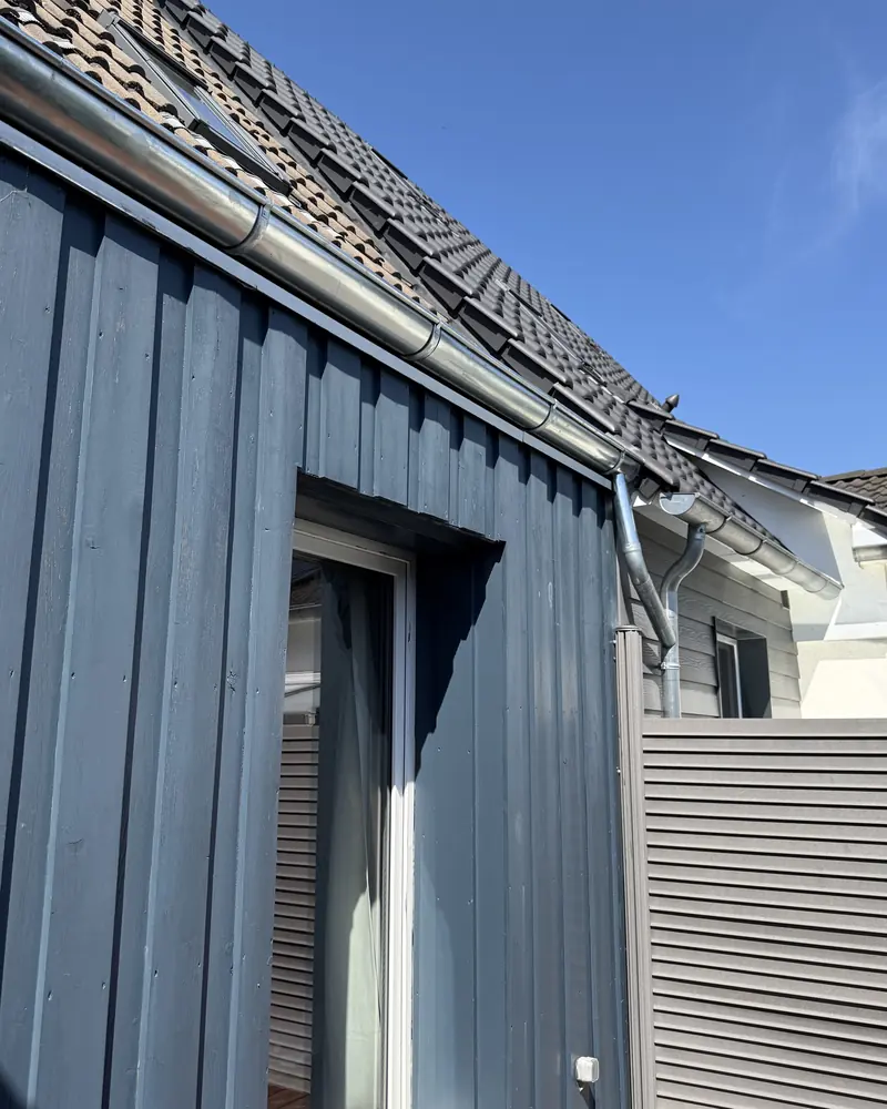 Graublau gestrichene Holzfassade mit Boden-Deckel-Schalung und neuer Dachrinne