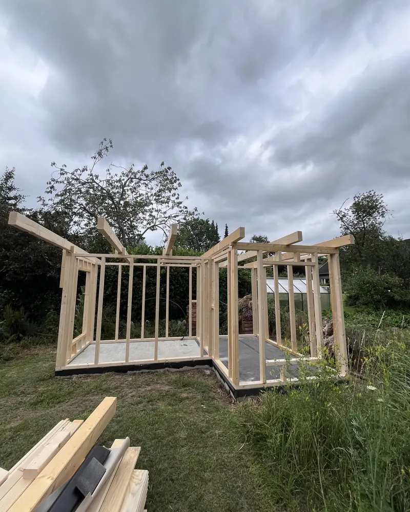 Aufgerichtetes Holzständerwerk eines Gartenhauses mit auskragenden Sparren