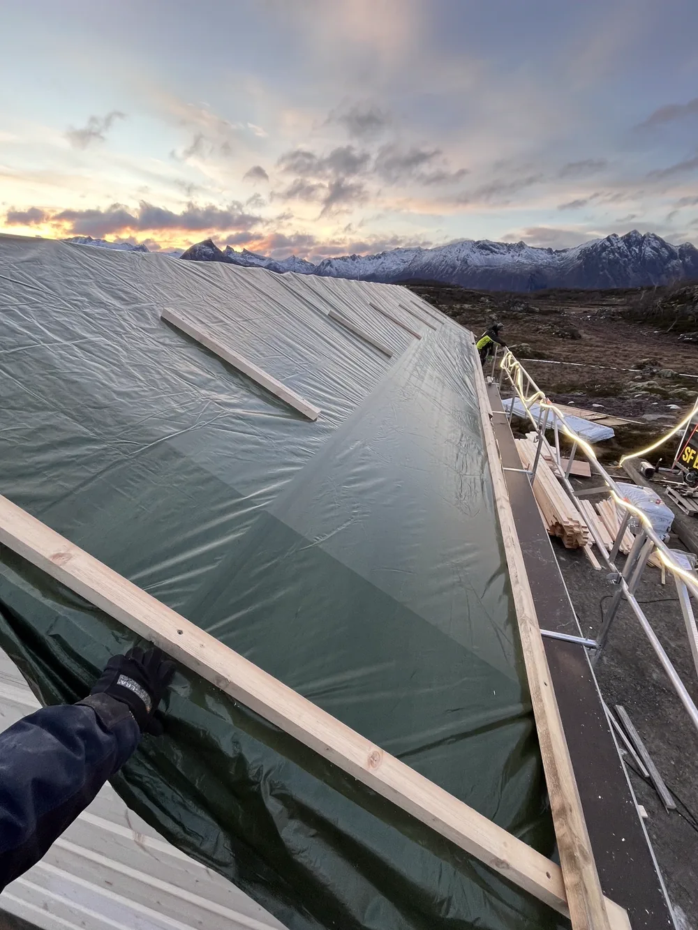 Dachfläche wird mit einer Schutzplane abgedeckt, Bergpanorama bei Sonnenuntergang