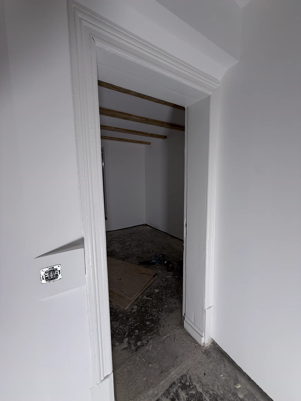 Blick durch eine neue Türöffnung in den Nebenraum mit Balkendecke