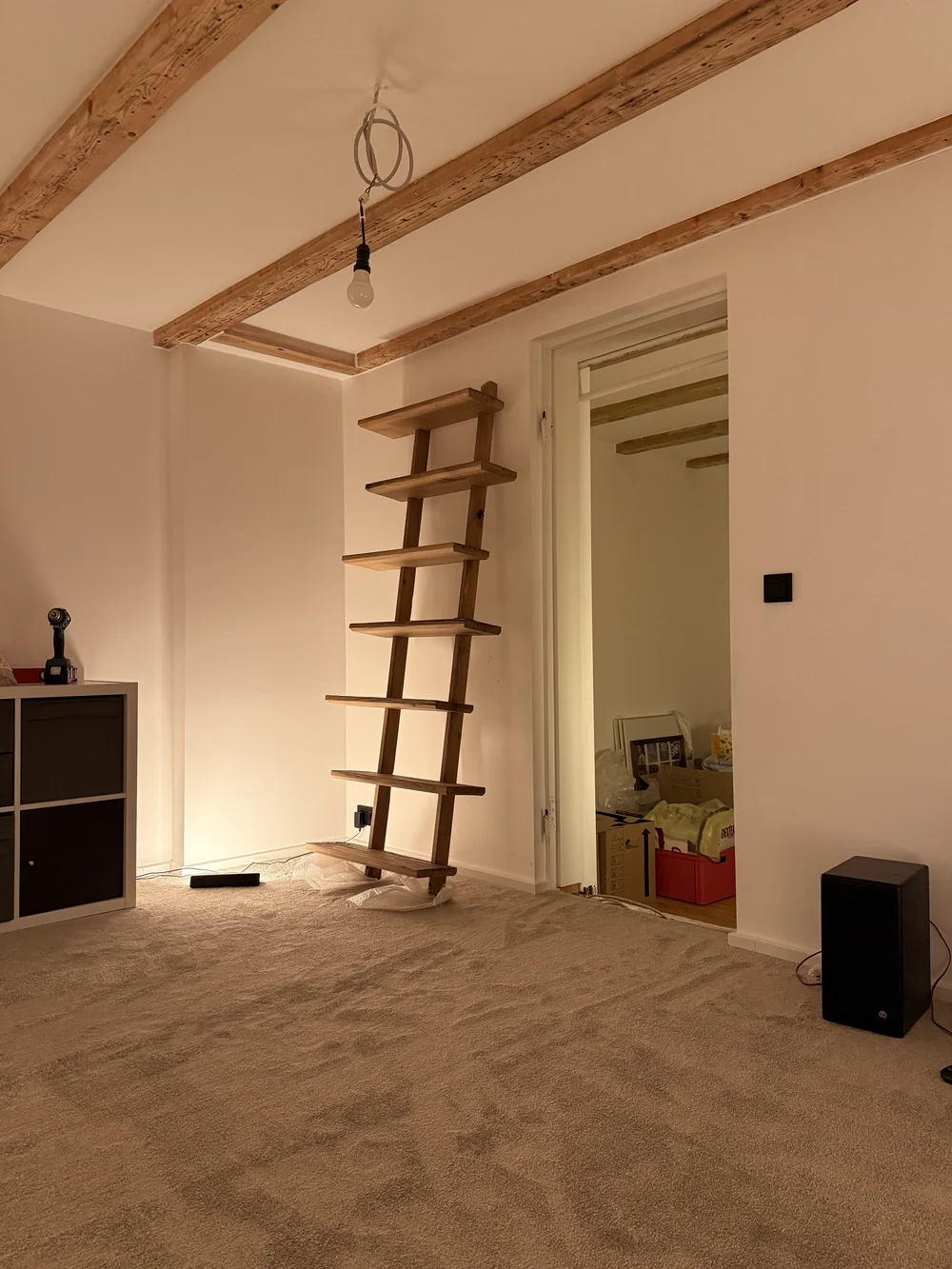 Fertig saniertes Zimmer mit freiliegendem Deckenbalken und handgefertigtem Holz-Wandregal