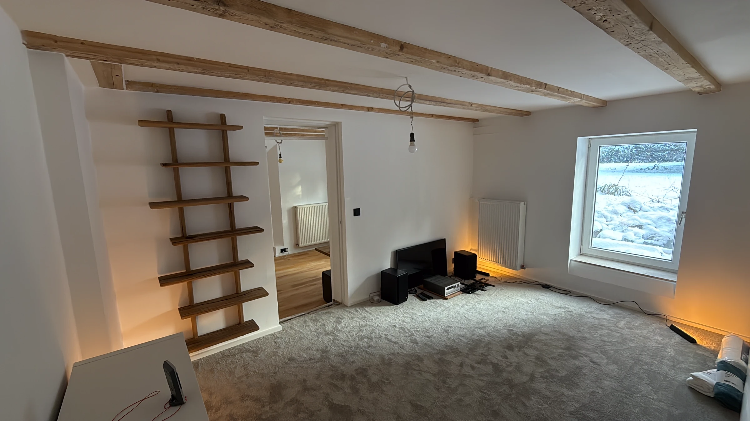 Sanierter Altbau-Wohnraum mit freiliegender Balkendecke und maßgefertigtem Holz-Wandregal